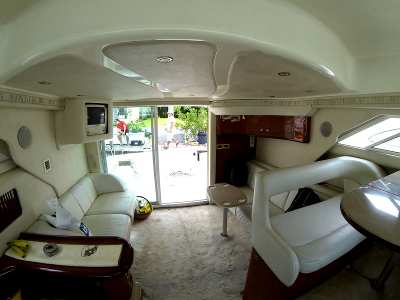 Salón interior del Sea Ray 44 con asientos de piel blanca, TV y cocineta, con la puerta corrediza abierta hacia el cockpit