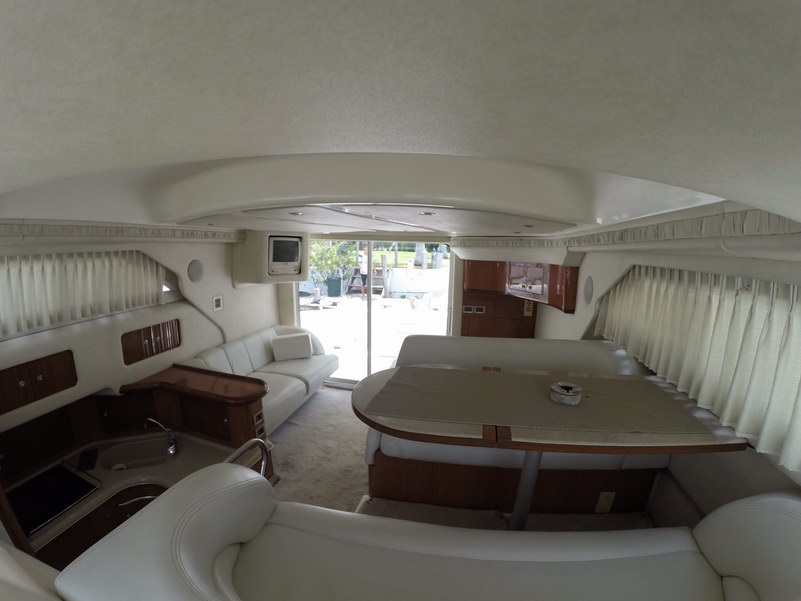Vista amplia del salón del Sea Ray 44 con asientos envolventes, una gran mesa convertible y cocineta bajo cubierta