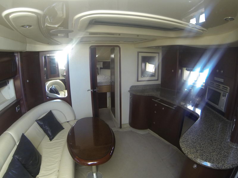 Interior salon of a Sea Ray Sundancer shot wide-angle: a white leather sofa with dark pillows, a glossy wood cocktail table, and a galley with granite counters and dark wood cabinetry to the right.