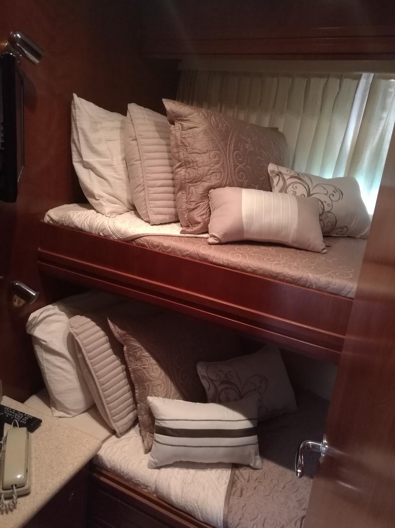 Twin bunk stateroom on Carver 55 ft yacht rental in Cancún with elegant bedding and rich mahogany woodwork trim