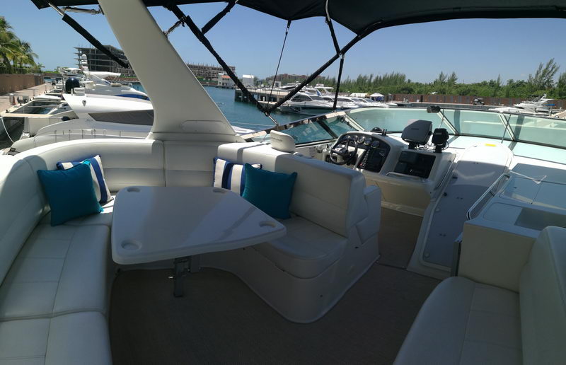 Fly bridge cockpit of Carver 55 ft yacht showing helm station and lounge seating with teal cushions at Cancún marina