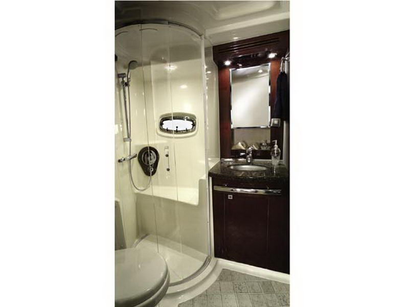 Bathroom aboard Sea Ray 55 ft luxury yacht with curved glass shower enclosure, granite vanity and dark wood cabinets