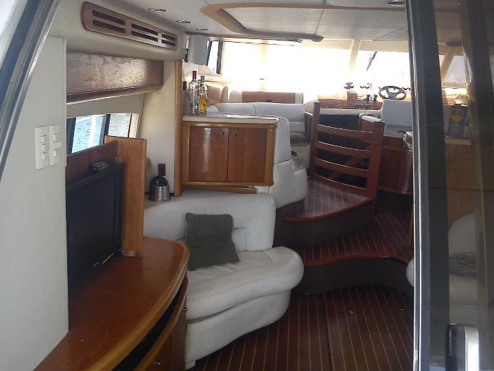 Interior salon of Sealine 55 ft yacht rental showing lounge seating, galley bar, teak floors and stairs to helm station