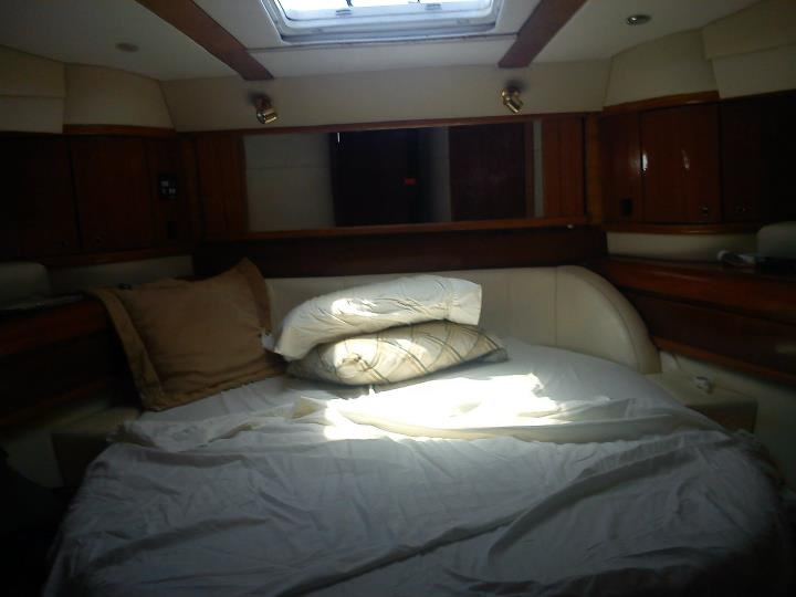 Forward stateroom of Sealine 55 ft group charter yacht with V-berth bed, overhead hatch and warm mahogany cabinetry