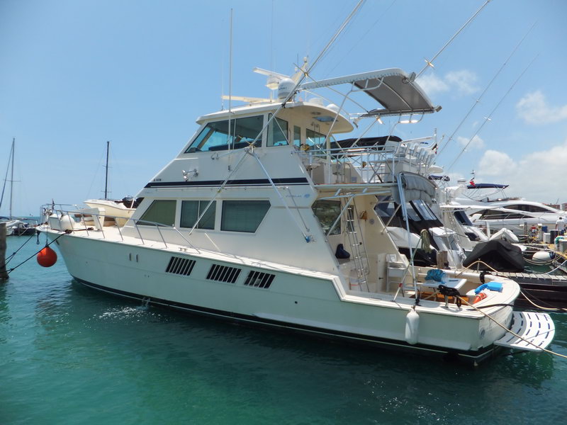 Hatteras 66 ft embarcación de pesca de altura, perfil exterior completo con puente de mando y outriggers en marina caribeña