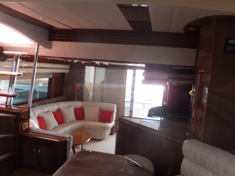 Second lounge of Nuvaris 63 ft yacht charter with curved cream sofa, red cushions, TV cabinet and natural ocean light