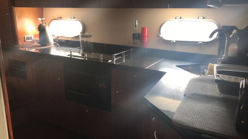 Galley kitchen of Sunseeker 64 ft yacht rental with black granite counters, porthole windows and espresso machine