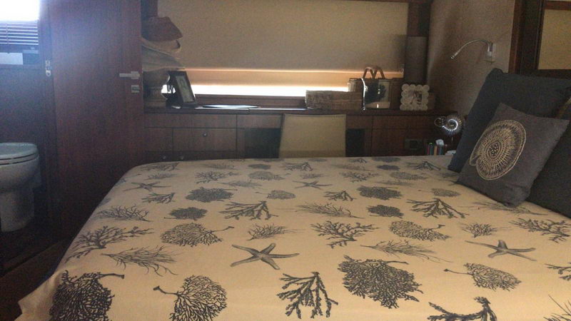 Second stateroom of Sunseeker 64 ft yacht rental with coral print bedding, lit headboard shelf and grey decorative cushions