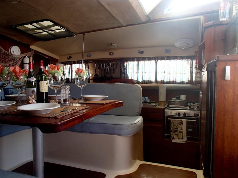 Comedor del catamarán de 32 pies con mesa servida, copas de vino y cocina equipada para un charter privado en Puerto Aventuras
