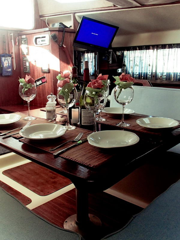Comedor interior del catamarán de 32 pies con mesa servida, copas y TV, listo para un charter privado en Puerto Aventuras