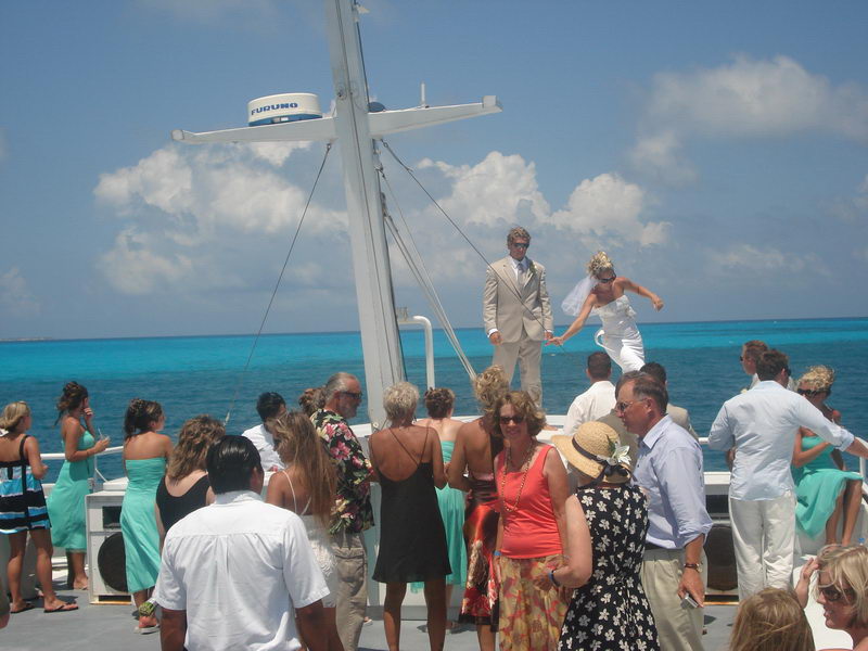 Groom in tan suit and bride in white gown reclining together on the white bow deck, deep blue and turquoise water behind. Nearly the same shot as wedding-21.