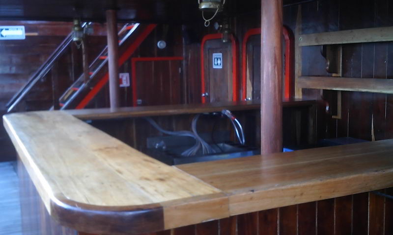 Barra de madera pulida en forma de L dentro del galeón Jolly Roger con paneles de ribete rojo y una escalera a la cubierta superior