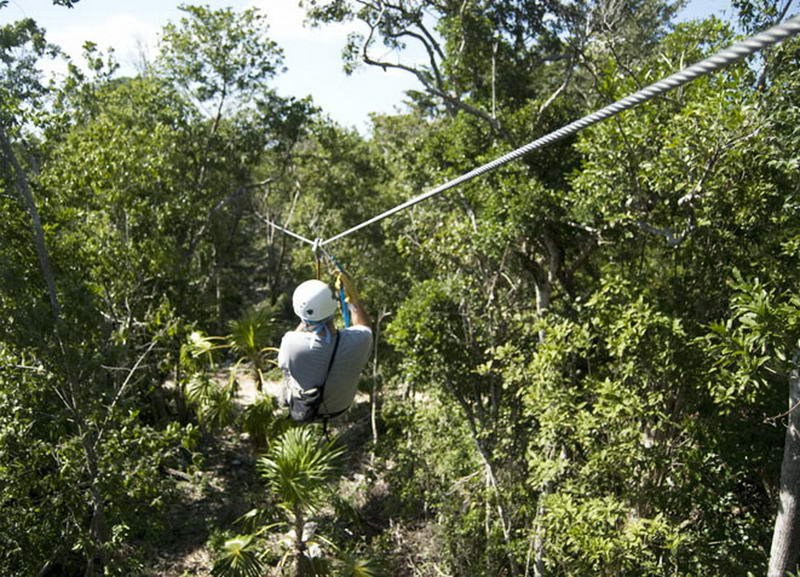 Visitante con casco blanco deslizándose en tirolesa sobre el denso dosel verde de la selva en Aktun Chen, Riviera Maya