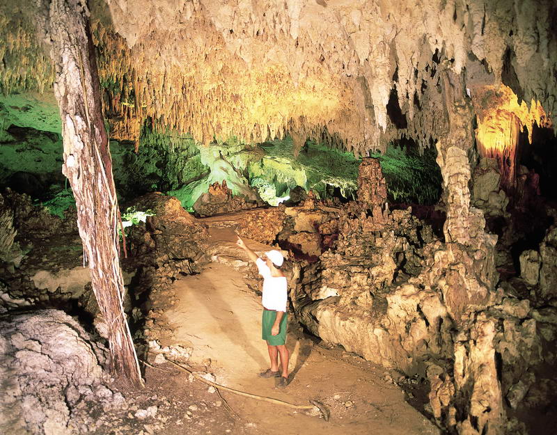 Guía señalando estalactitas iluminadas a lo largo del sendero de la cueva seca en el parque natural Aktun Chen, Riviera Maya