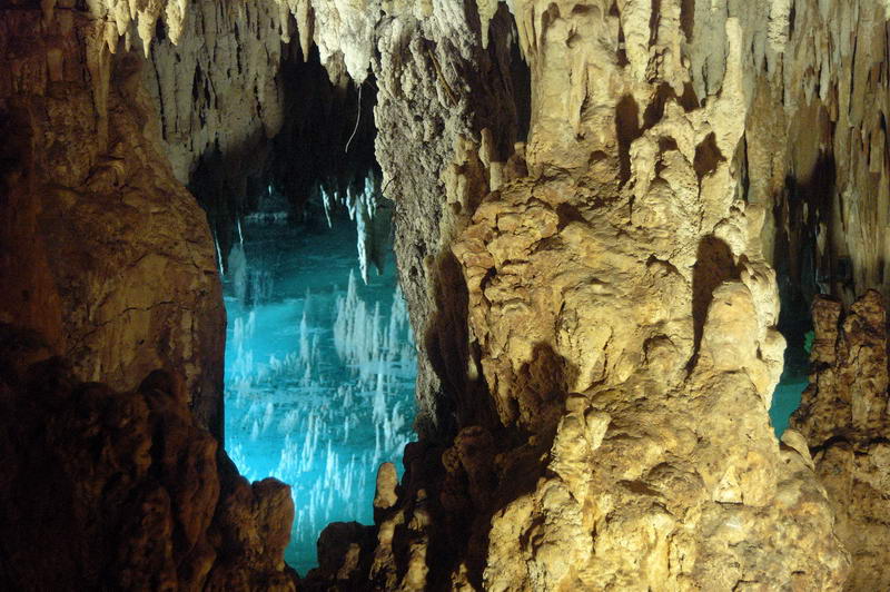 Dramáticas formaciones de estalactitas y estalagmitas que enmarcan el resplandeciente cenote azul subterráneo dentro de la cueva Aktun Chen