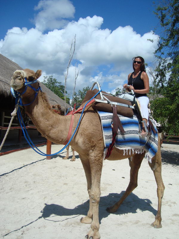 Mujer sentada en un camello ensillado junto a palapas de palma en el rancho del safari en camello de 