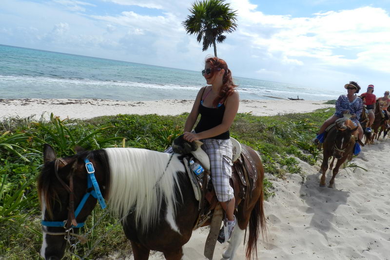 Jinetes cruzando la arena blanca de Playa Maroma cerca de Playa del Carmen en un tour guiado a caballo