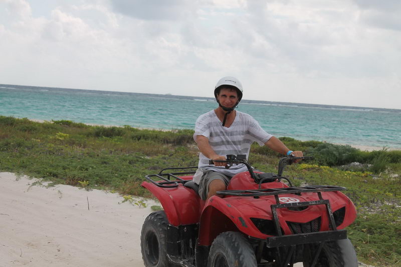 Conductor con casco en una cuatrimoto roja por un sendero de arena junto al Caribe turquesa en Playa Maroma
