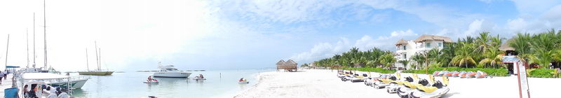 Vista panorámica de Playa Maroma con yates en la marina, motos acuáticas sobre la arena blanca y mar Caribe turquesa, Riviera Maya