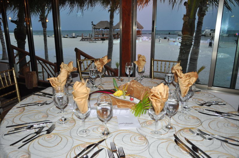 Mesa de banquete con servilletas doradas frente a la playa de arena blanca al atardecer en el restaurante de Maroma, Riviera Maya
