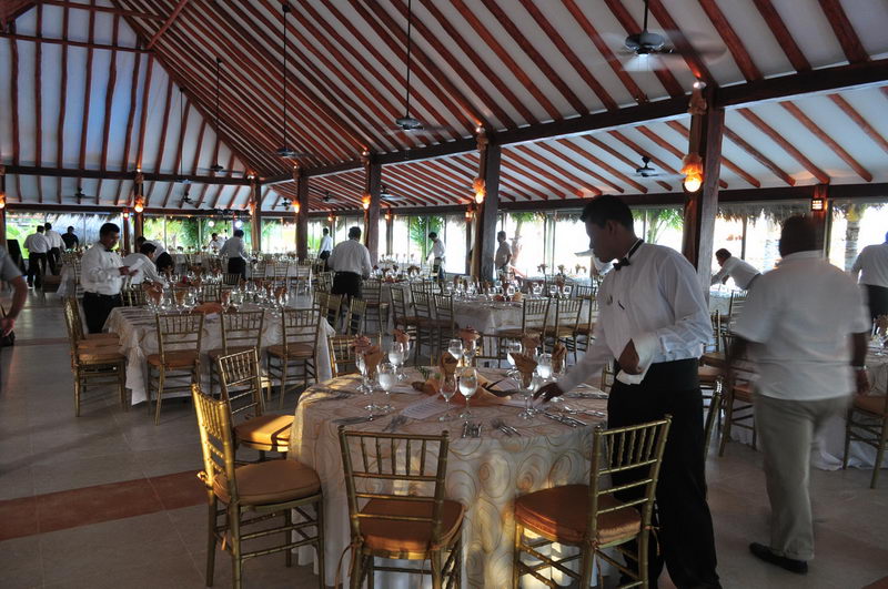 Meseros acomodando los cubiertos en mesas redondas antes de una cena de gala bajo la palapa del restaurante de Maroma, Riviera Maya