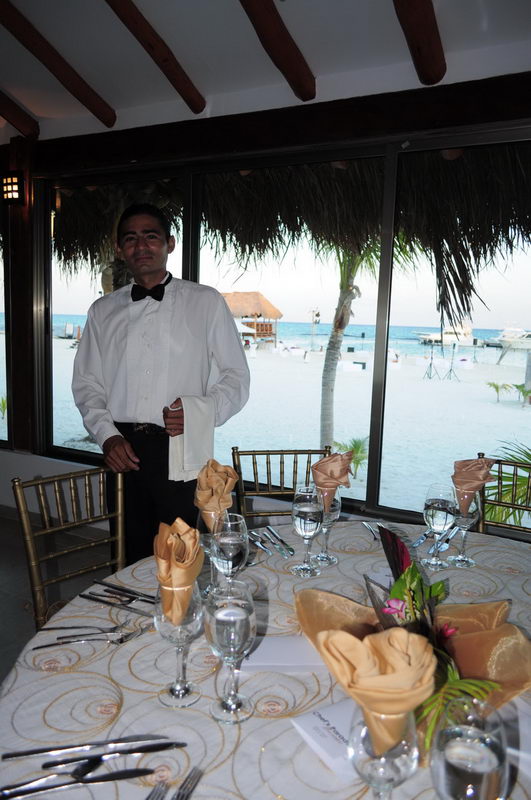 Mesero con corbatín junto a una mesa de banquete elegante con vista al mar Caribe en el restaurante de Maroma, Riviera Maya