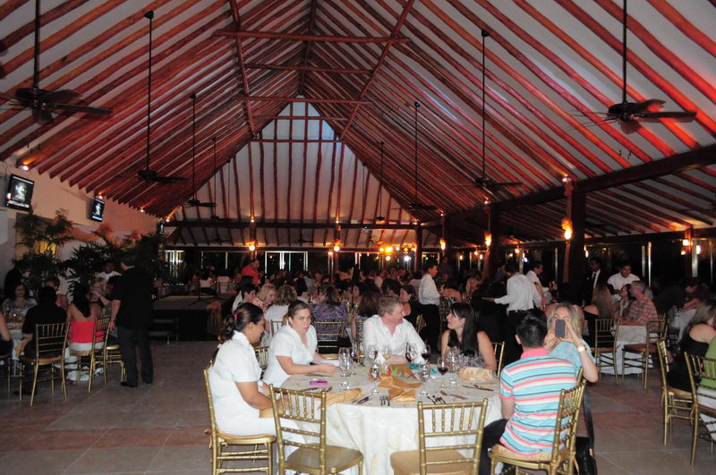 Invitados cenando en mesas redondas bajo el amplio techo de palapa durante un evento de grupo en el restaurante de Maroma, Riviera Maya