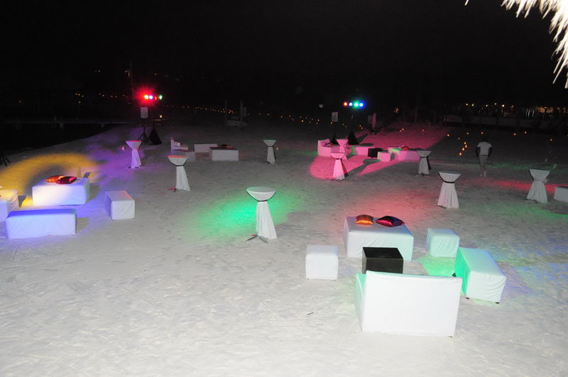 Evento privado nocturno en la playa con salas lounge blancas, mesas altas y luces de fiesta sobre la arena en Marina Maroma, Riviera Maya
