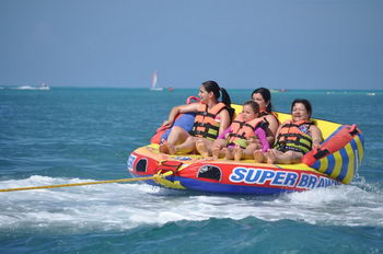 Riders bouncing on an inflatable towable doughnut tube behind a boat on the turquoise Cancun sea