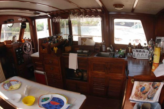 Cozy wood-paneled interior salon of Tafil 40 ft trawler with steering wheel, fully equipped galley kitchen and dining table